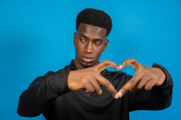 Young man making heart shape with hands on blue background