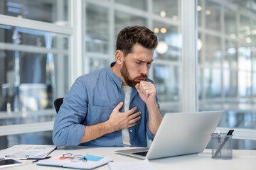 Fototapeta premium A male professional experiencing discomfort in his chest as he coughs while at work in an office. This image conveys health-related struggles in a business environment.