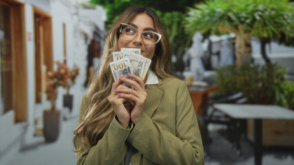 Business woman fanning a stack of dollar banknotes with her hands at outdoor cafe; wealth...