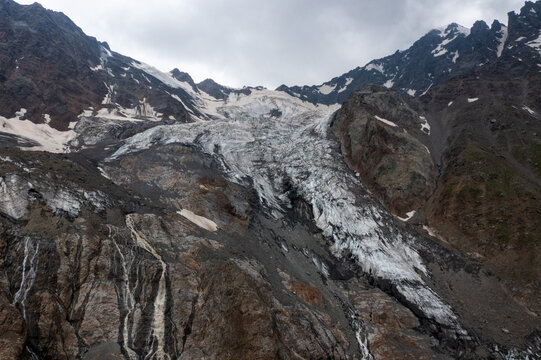 Aerial view of the glacier cascading down the rugged mountain slopes, a frozen river amidst the stark, rocky landscape, Altai Republic, Russia.