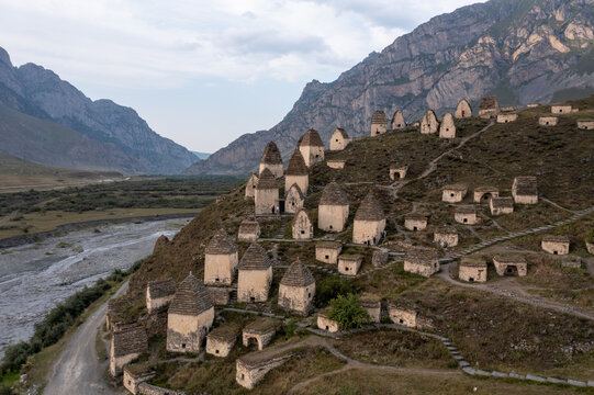 Aerial view of Dargavs, the City of the Dead, with its ancient stone crypts clinging to the hillside, nestled beneath the watchful gaze of the Caucasus Mountains, North Ossetia, Russia.