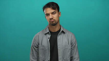 Obraz premium Young hispanic man in casual attire stands in front of an isolated vibrant green background, expressing a pensive and relaxed demeanor with closed eyes and neutral expression.