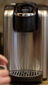 Close-up of a hand carefully placing a fresh pod into a modern single-serve coffee machine before pressing the brew button for a perfect cup.