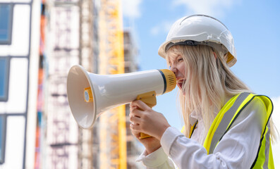 Portrait of young woman construction worker in vivid safety gear uses a megaphone to communicate...