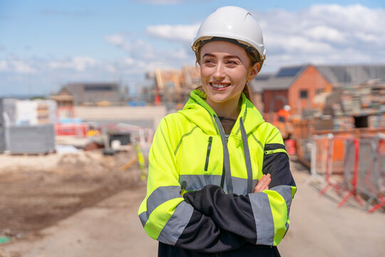 Portrait of smiling young woman builder in bright safety gear and hard hat at construction site