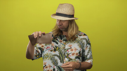 Blond man with long hair straw hat and floral shirt checking wallet with both hands in a studio;...