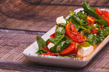 Person dressing a salad of tomato, fresh cheese and spinach.