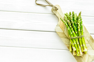 Cooking asparagus. Bunch steams on cutting board on white wooden background top-down copy space