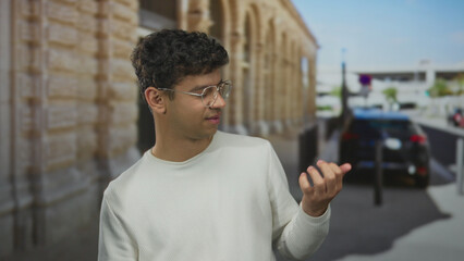 Man wearing glasses playing air guitar with bare hands on a sunny historic city street; joy leisure.