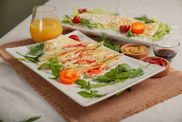 Wheat flatbread with vegetables and meat baked grilled on white plate on served table