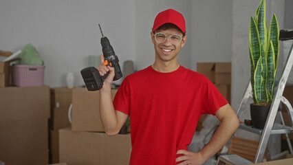 Man grips power drill with one hand and rests his other hand on hip amid moving boxes in building...