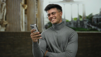 Young man smiling at smartphone with roman ruins in background, showcasing modern technology...
