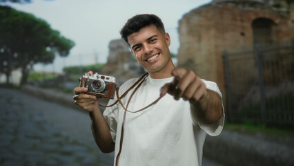 Young man smiling with a vintage camera on a city street outdoors, exuding a lively and attractive vibe.