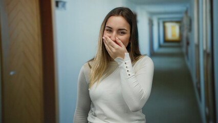 Woman smiling in a hotel hallway with casual attire and blonde hair, conveying a sense of warmth and comfort in an inviting indoor atmosphere.