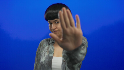 Young chinese woman showing stop gesture with palm against isolated blue background, expressing...