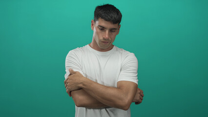 Man holds arm in front of green background in studio, gripping his visible forearm with downcast...