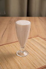 Creamy chocolate cocktail in a tall glass goblet on a light wooden table