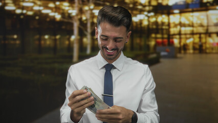 Man counting dirham banknotes on street in front of illuminated city building facade at night; prosperity.