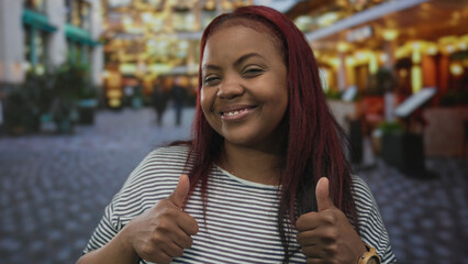Woman smiling and giving thumbs up hand gesture on busy city street lined with stores and...