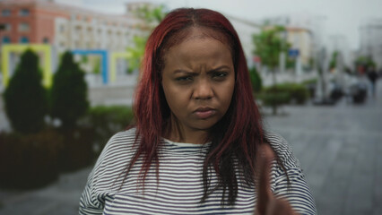 African american woman points finger sternly on street lined with parked cars and potted trees;...