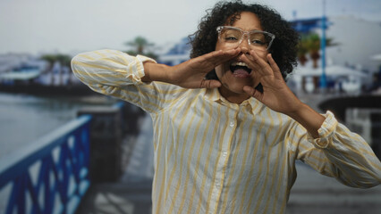 Woman with hands raised in dance on street near seaside walkway under gentle morning sunlight;...