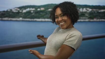 Woman extends bare arms and gestures open palm toward ocean view at seaside building under...