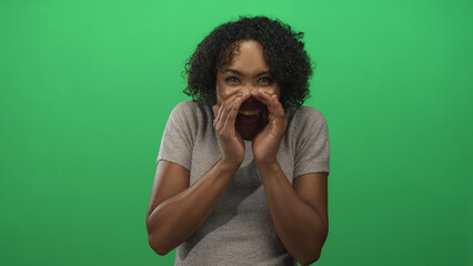 Woman cupping hands around mouth in studio setting with bright green background; attention...