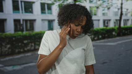 African american woman in white tshirt pressing cheek against building facade on street pavement;...