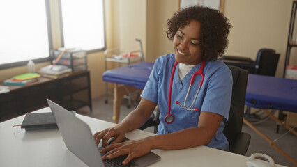 Woman doctor types on laptop inside a building with a red stethoscope around her neck and an exam...