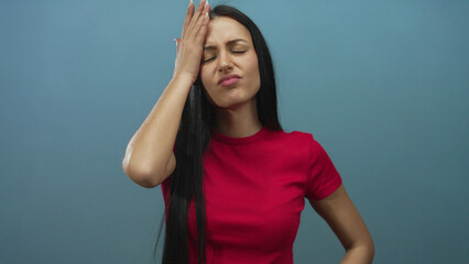 Woman with long hair in red shirt frowning and inspecting split ends against isolated blue...