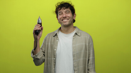 Hispanic man holding screwdriver against a vibrant yellow background while smiling.