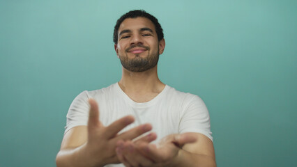 Smiling man extends bare hands in turquoise studio with direct gaze offering gesture; welcome...