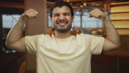 Man flexes arms in a building restaurant hall wearing a white t shirt; confidence strength...