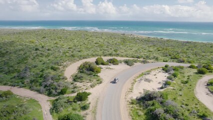 Vacation Car On Winding Road Towards Pristine Ocean - Aerial Drone Shot