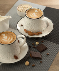 Cappuccino in white cups with saucer and nuts on table in coffee shop