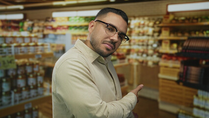 Man beckons with palm forward in a colorful supermarket building aisle filled with shelves;...