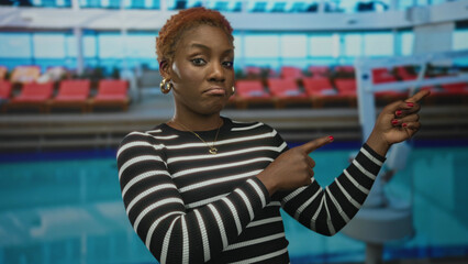 Woman in loose striped black sweater with red nails points finger at object in building; skepticism.