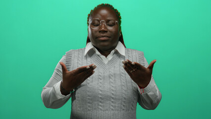 Woman meditating indoors over a green wall background, wearing a white shirt and glasses,...