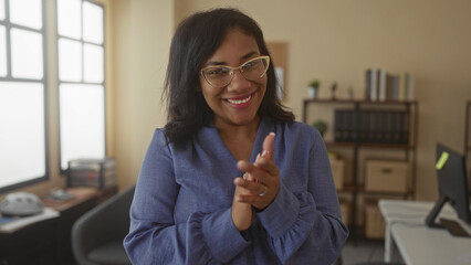 Woman pointing finger at camera in office building, wearing glasses and blue blouse and standing...