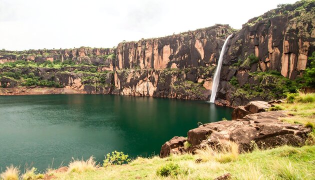Majestic Waterfall Plunging into Emerald Lake Surrounded by Rocky Cliffs and Lush Greenery