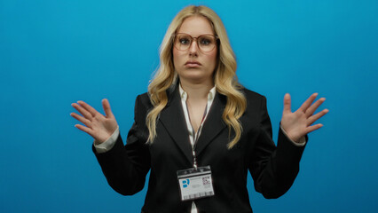 Woman gesturing frustratedly against a blue background wearing a business suit and glasses, displaying an id badge, conveying urgency and tension in a professional setting.