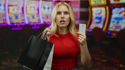 Blonde woman with shopping bags stands surprised in a casino surrounded by slot machines holding a...
