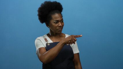 Woman wearing apron points confidently against blue background, embodying focus and direction in an...