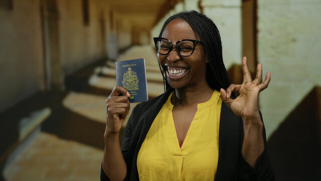 Woman smiling in an academic setting with canadian passport, dressed in yellow, embodying success and multiculturalism, standing confidently in a university corridor.