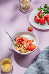 Granola or muesli with natural greek yogurt, strawberry and honey in a bowl on a violet background