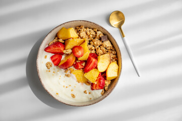 Granola or muesli with natural greek yogurt, strawberry and peach in a bowl on a white background