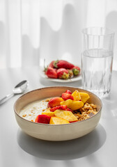 Granola or muesli with natural greek yogurt, strawberry and peach in a bowl on a white table near...