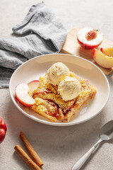 Peach crumble or cobbler with vanilla ice cream scoops and cinnamon on a plate on a light background