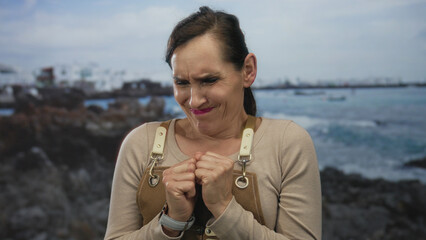 Woman wearing apron stands on a rocky seaside with an expression of various emotions, set against a...