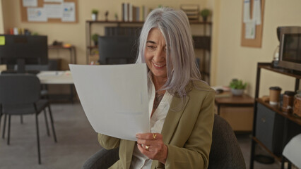 Woman reviewing document in modern office with grey hair and focused expression, showcasing...